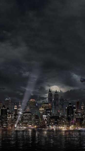 Gotham skyline at night with bright city lights and a full moon reflecting on the water