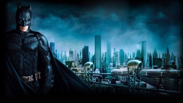 Batman standing in front of the Gotham skyline at night with a dark cloudy sky