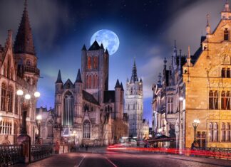 The street showcases gothic architecture with illuminated historic buildings under a bright full moon, 4K Desktop Wallpaper