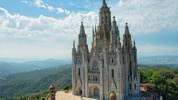 A gothic church stands tall above lush green mountains under a blue sky in Spain Wallpapers, HD Desktop Wallpaper