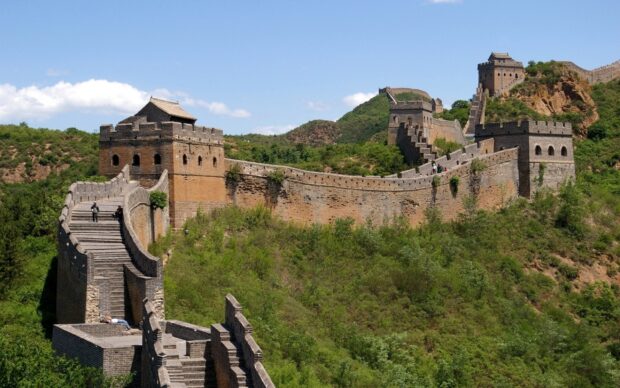 A historic section of Great Wall of China winding through green hills under a clear blue sky
