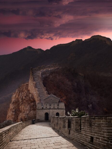 Ancient Great Wall of China winding through mountainous terrain at sunset with dramatic clouds