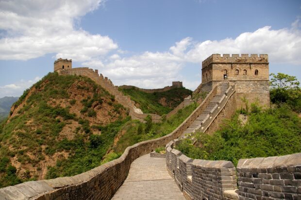 Ancient section of the Great Wall of China winding over green hills under a partly cloudy sky