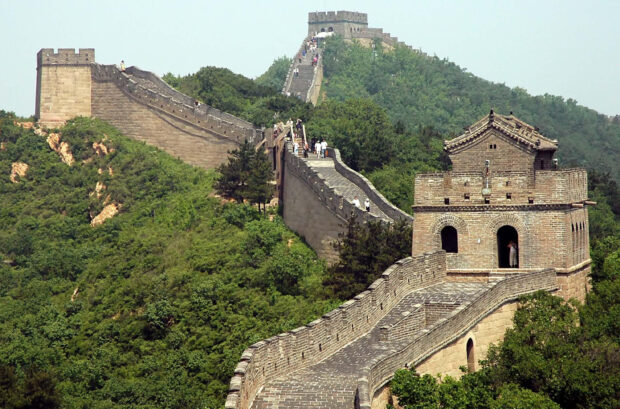 Great Wall Of China winding through green hills with visitors walking along the stone pathway