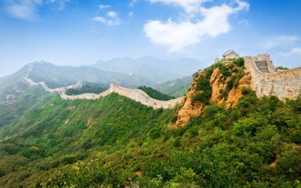 The Great Wall of China winding across lush green hills under a bright blue sky