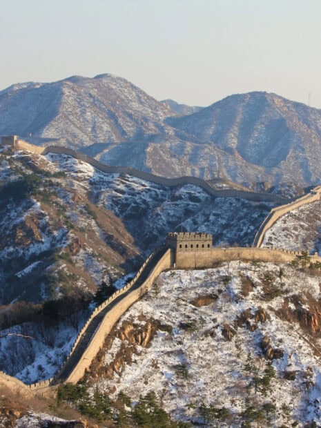 Snow covered Great Wall of China winding through mountainous landscape in winter