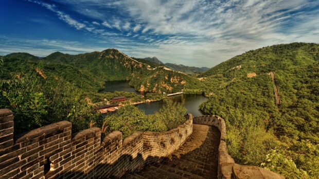 A scenic view of the Great Wall of China surrounded by lush green mountains and a calm river