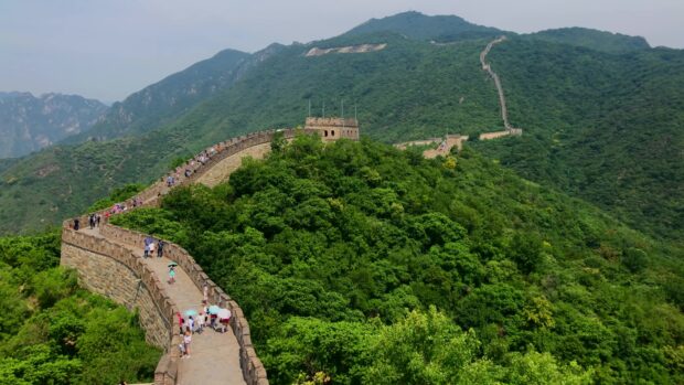 A scenic view of the Great Wall of China winding through lush green mountains with visitors walking along the path
