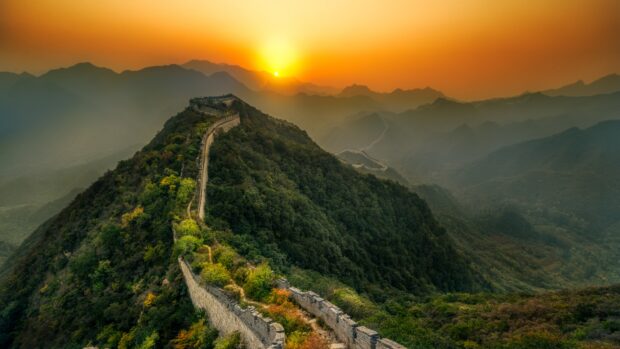 Great Wall of China winding through green hills at sunset with vibrant orange sky