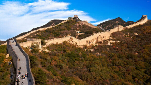 The Great Wall of China stretches over lush hills under a bright blue sky with visitors walking along the path