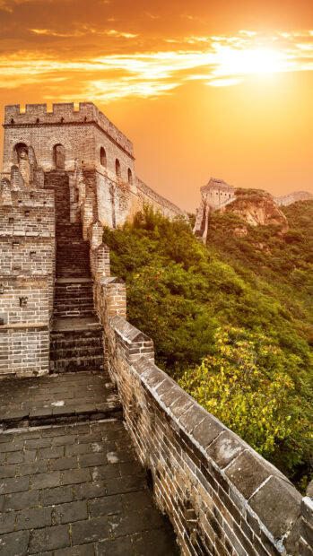 The great wall of china stretches over lush green hills under a vibrant sunset sky