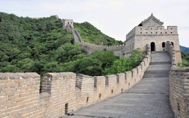 The Great Wall of China stretches over green hills with ancient stone architecture