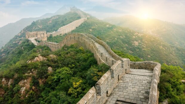 The Great Wall of China stretching over green hills during sunrise with clear sky and ancient stone structure