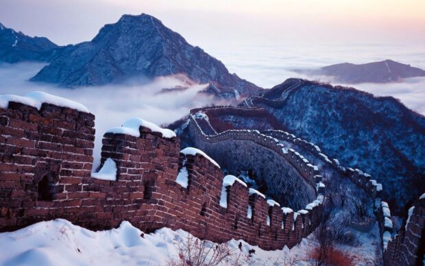 Snow covered Great Wall of China winding through mountainous terrain in winter haze