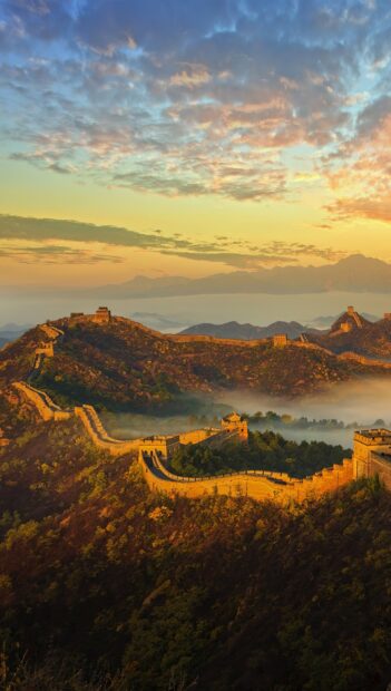Great wall of China stretches over hills under a colorful sky at sunrise