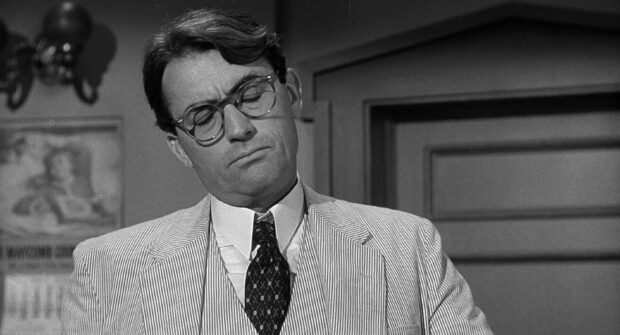 Gregory Peck in a striped suit and glasses looks thoughtful in a black and white scene, 2K Desktop Wallpaper