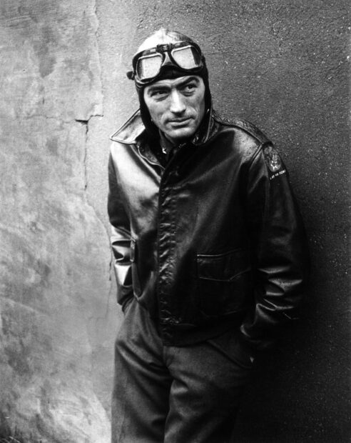 A black and white portrait of Gregory Peck wearing a leather jacket and pilot goggles leaning against a wall, 2K Mobile Wallpaper