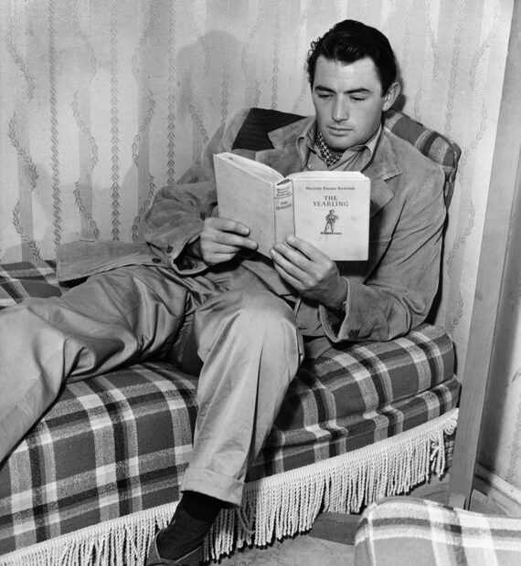 Gregory Peck is sitting on a plaid couch reading a book titled The Yearling, HD Desktop Wallpaper
