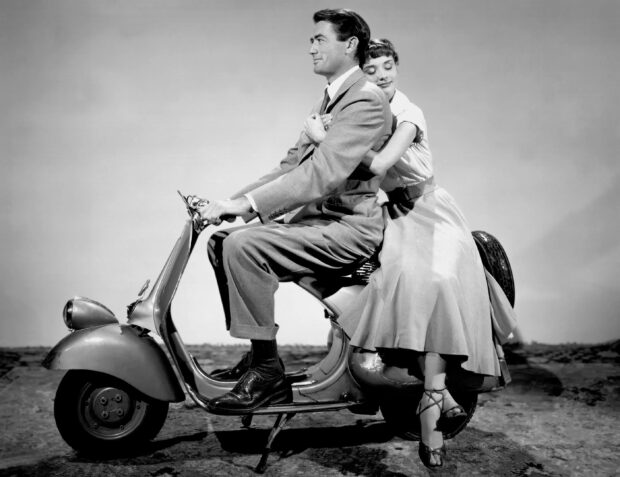 Gregory Peck embraces woman while riding a vintage scooter in black and white, 2K Desktop Wallpaper