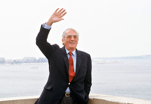 Gregory Peck smiles and waves while standing near the coast wearing a suit and red tie, HD Desktop Wallpaper