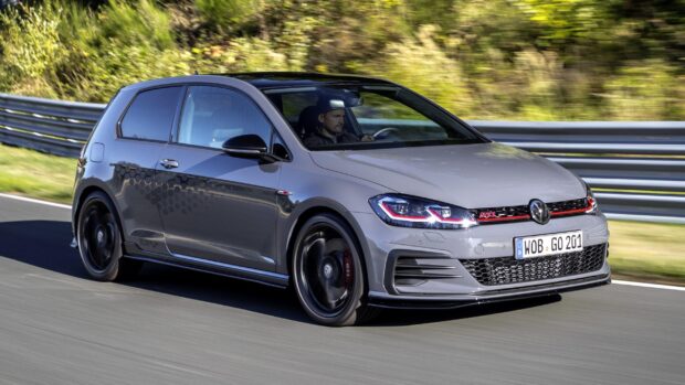 A sporty gray gti car driving fast on a race track with greenery in the background