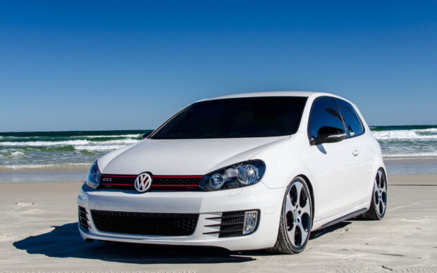 White Volkswagen Gti parked on sandy beach under clear blue sky