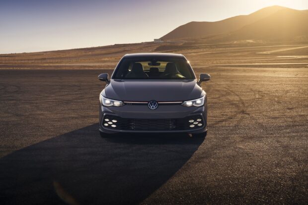 Front view of a modern GTI sports car parked on an open asphalt area at sunset
