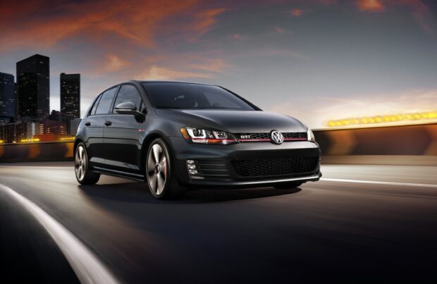 A sleek black GTI car driving fast on a city highway during sunset