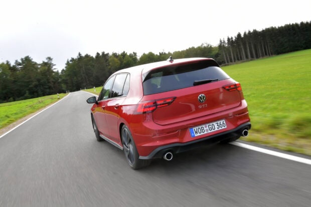 Red Volkswagen Gti driving on a forest road with green grass on the side