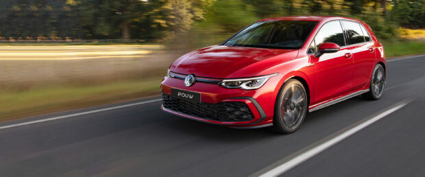Red Volkswagen Gti driving fast on a blurred road with green trees in the background