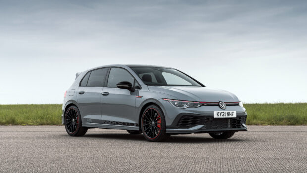Gray sporty Gti car parked on asphalt next to a grassy field in daylight