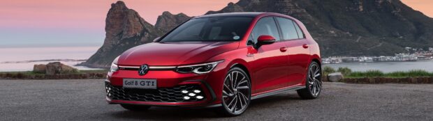 Red Volkswagen Golf 8 GTI parked near the coast with mountains in the background