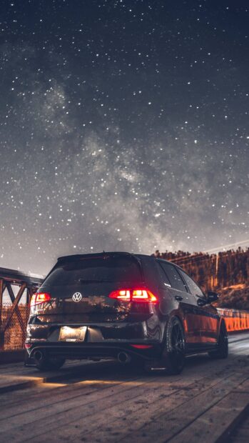 Black Gti car parked under a starry night sky on a wooden bridge