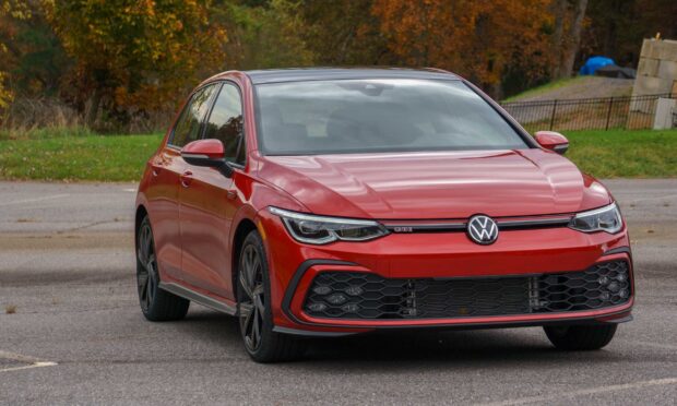Red Volkswagen Gti parked on the road with autumn trees in the background
