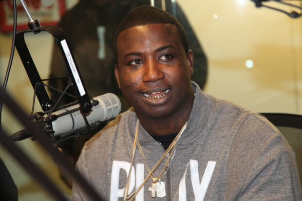 Gucci Mane wearing chains and a gray hoodie speaking into a microphone in a recording studio