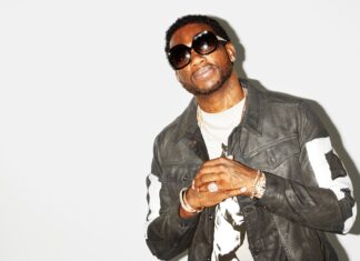 Gucci Mane wearing sunglasses and a leather jacket posing against a white background