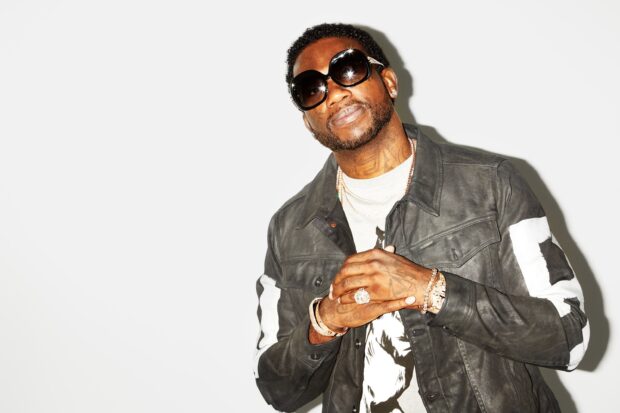 Gucci Mane wearing sunglasses and a leather jacket posing against a white background