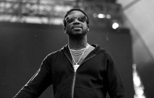 Gucci Mane wearing sunglasses and chains performing on stage with a confident expression