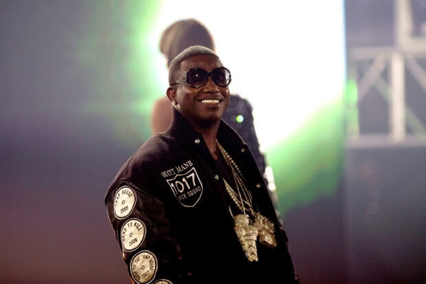 Gucci Mane wearing sunglasses and jewelry while smiling on stage
