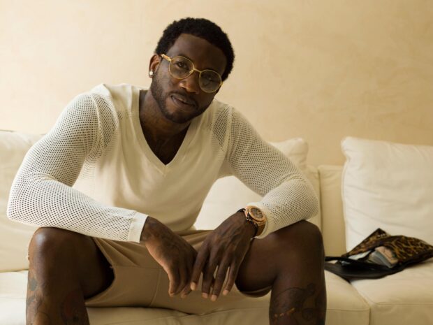 Gucci Mane wearing glasses and a white sweater sitting on a couch indoors