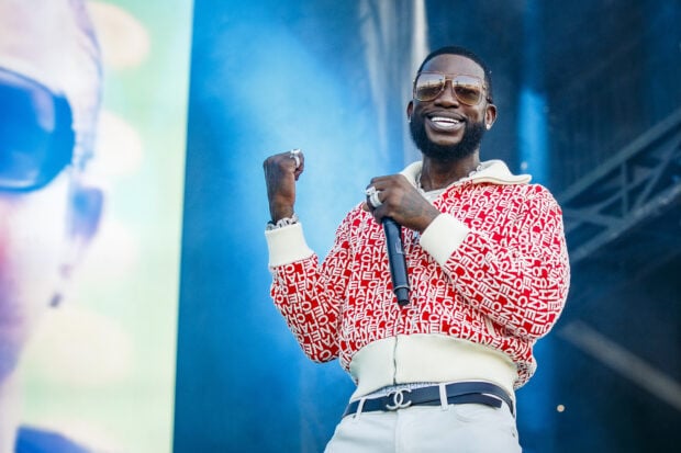 Gucci Mane performing on stage wearing a red and white jacket with sunglasses smiling