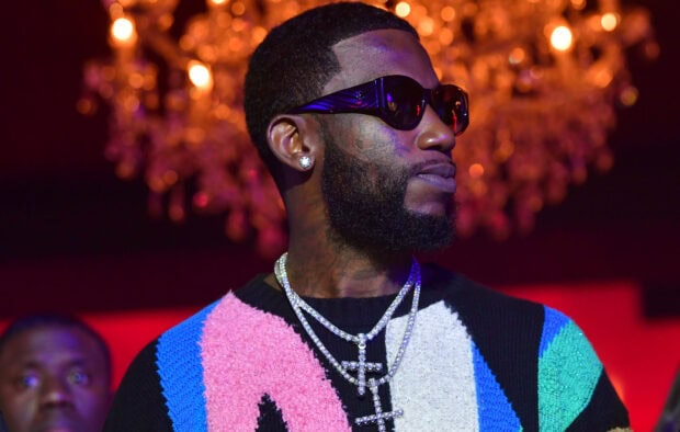 Gucci Mane wearing sunglasses and jewelry at a colorful event