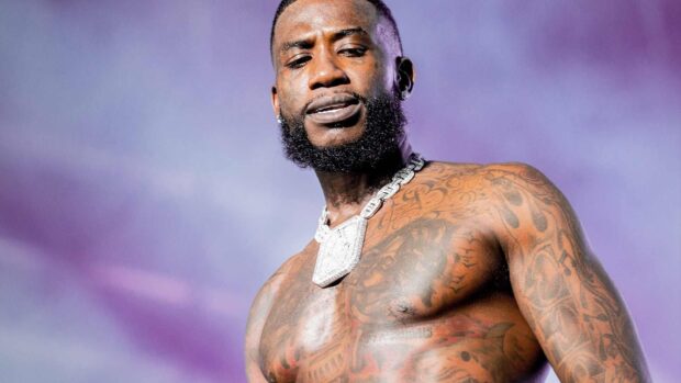 Gucci Mane showing his tattoos and chain on stage with a purple background