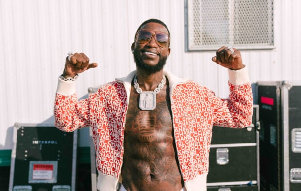 Gucci Mane smiling and posing shirtless with tattoos and jewelry outdoors