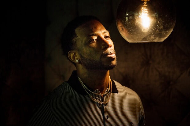 Gucci Mane looking thoughtfully under warm light in a striped shirt