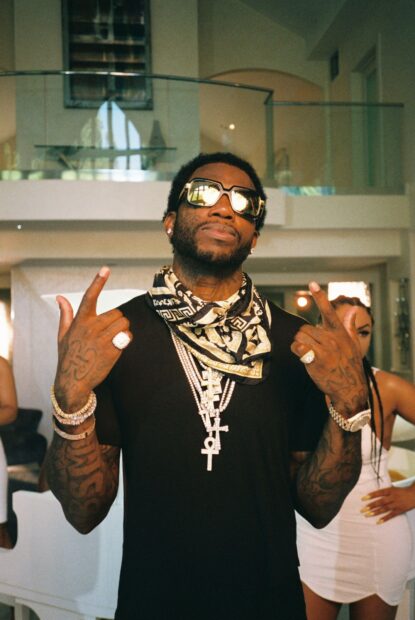 Gucci Mane wearing sunglasses and jewelry posing indoors with tattoos visible on his arms