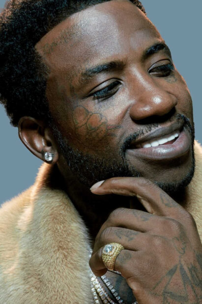 Gucci Mane showing a thoughtful smile with a fur coat and diamond ring