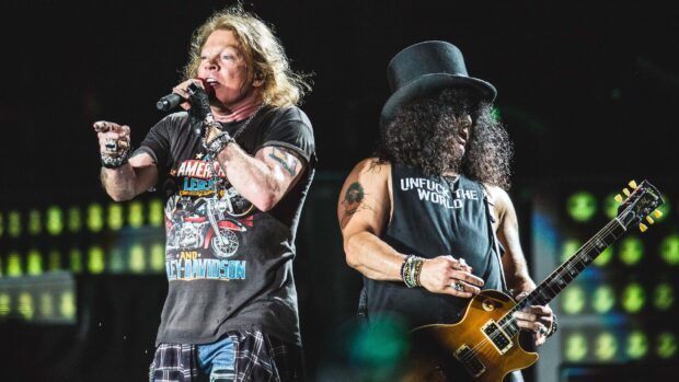Guns N Roses band members performing live on stage with guitar and microphone in a concert setting