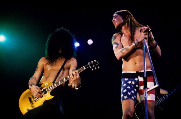 Guns N Roses performing live on stage with guitar and microphone in a rock concert setting