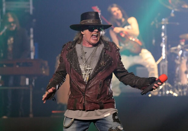 Guns N Roses singer performing on stage wearing a hat and leather jacket with microphone